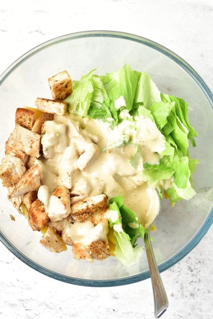 Caesar salad dressing drizzled over romaine lettuce, and cooked chicken pieces.