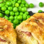 Cut chicken cordon bleu with green peas on white plate