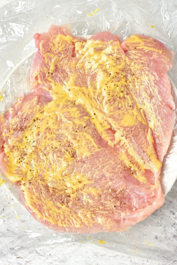 Pounded chicken fillets spread with mustard and seasoned with black pepper