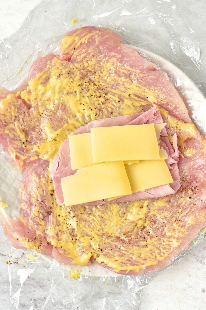 Chicken fillets spread with mustard, and topped with slices of ham and cheese