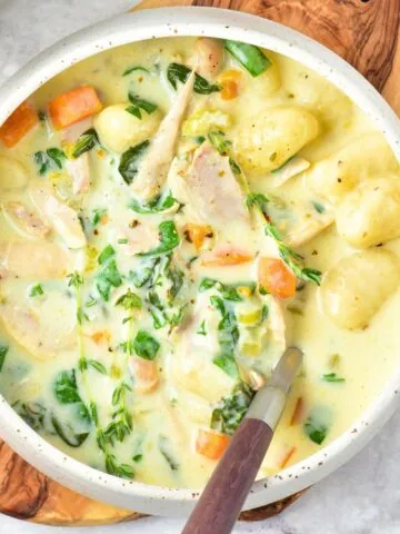 A bowl of chicken gnocchi soup on wooden board