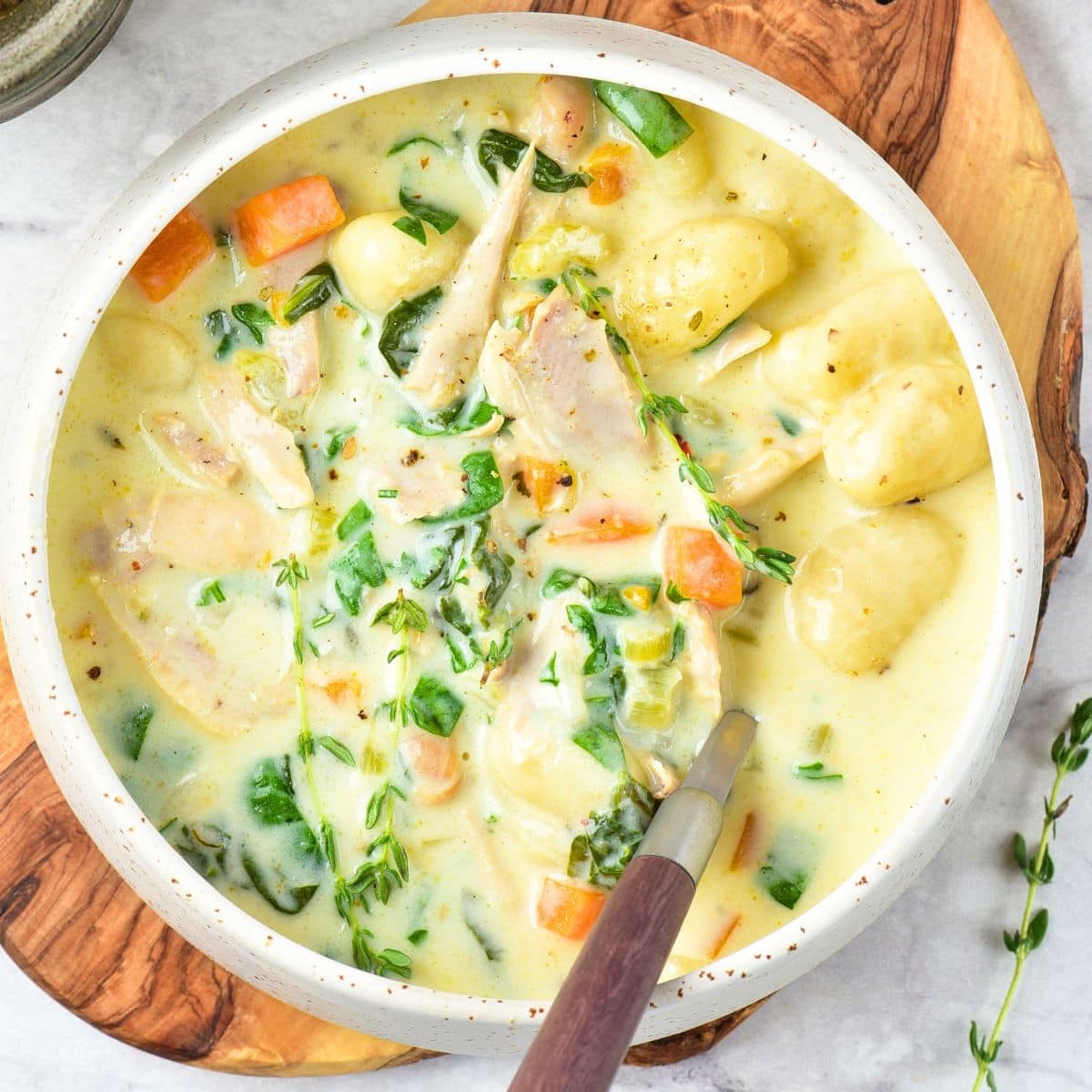 A bowl of chicken gnocchi soup on wooden board