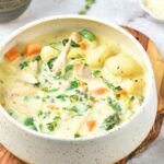 A bowl of chicken gnocchi soup on a wooden board.