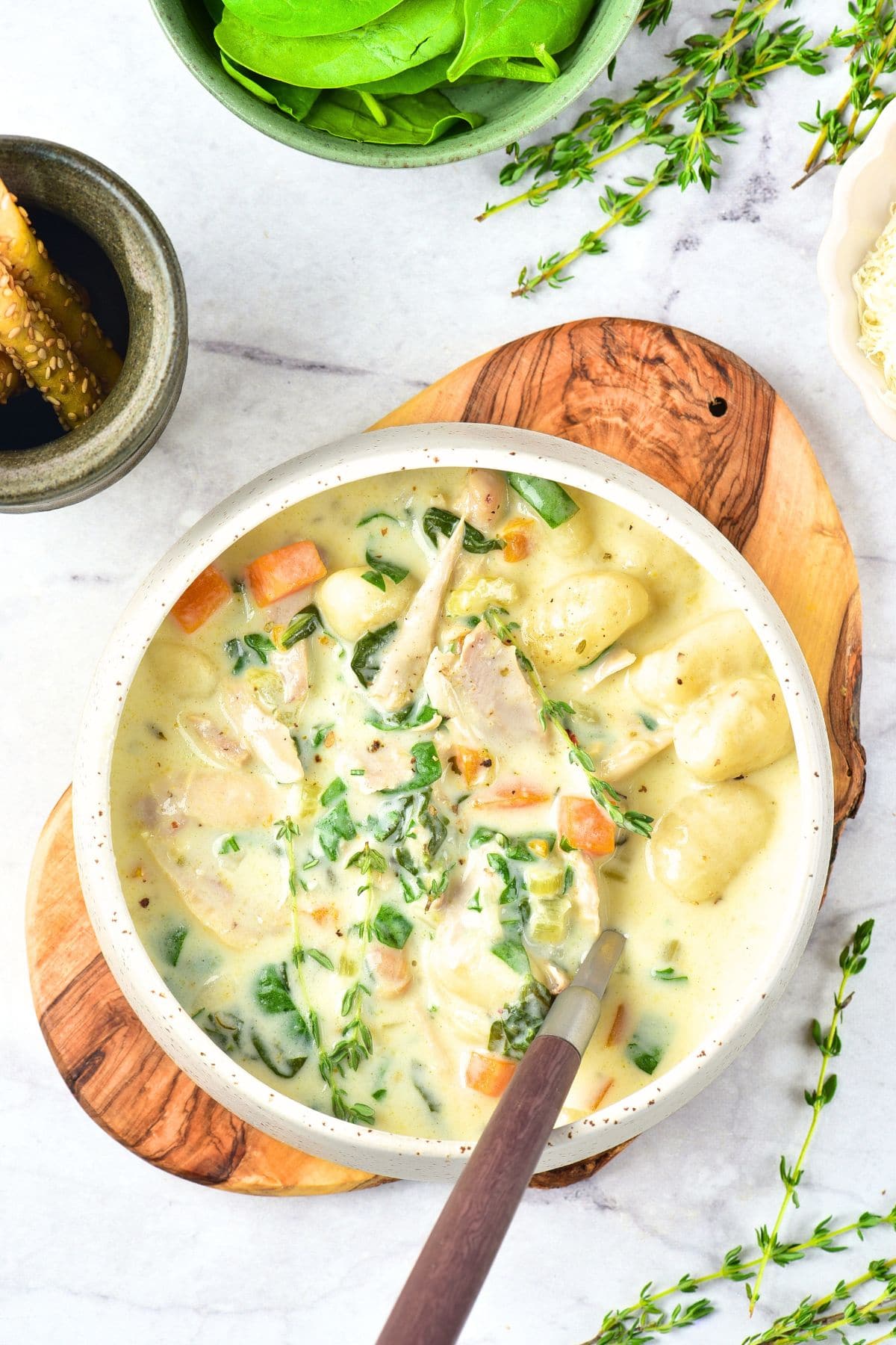 A bowl of chicken and gnocchi soup on top of wooden board.