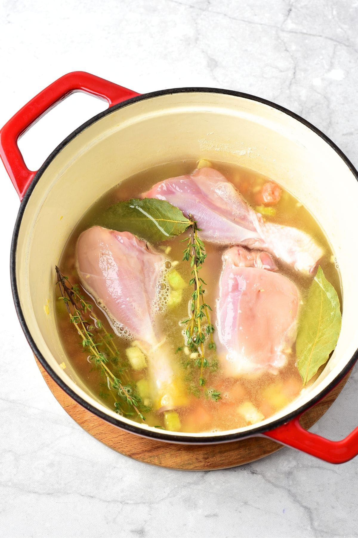 Chicken drumsticks, herbs, broth and veggies in Dutch oven.