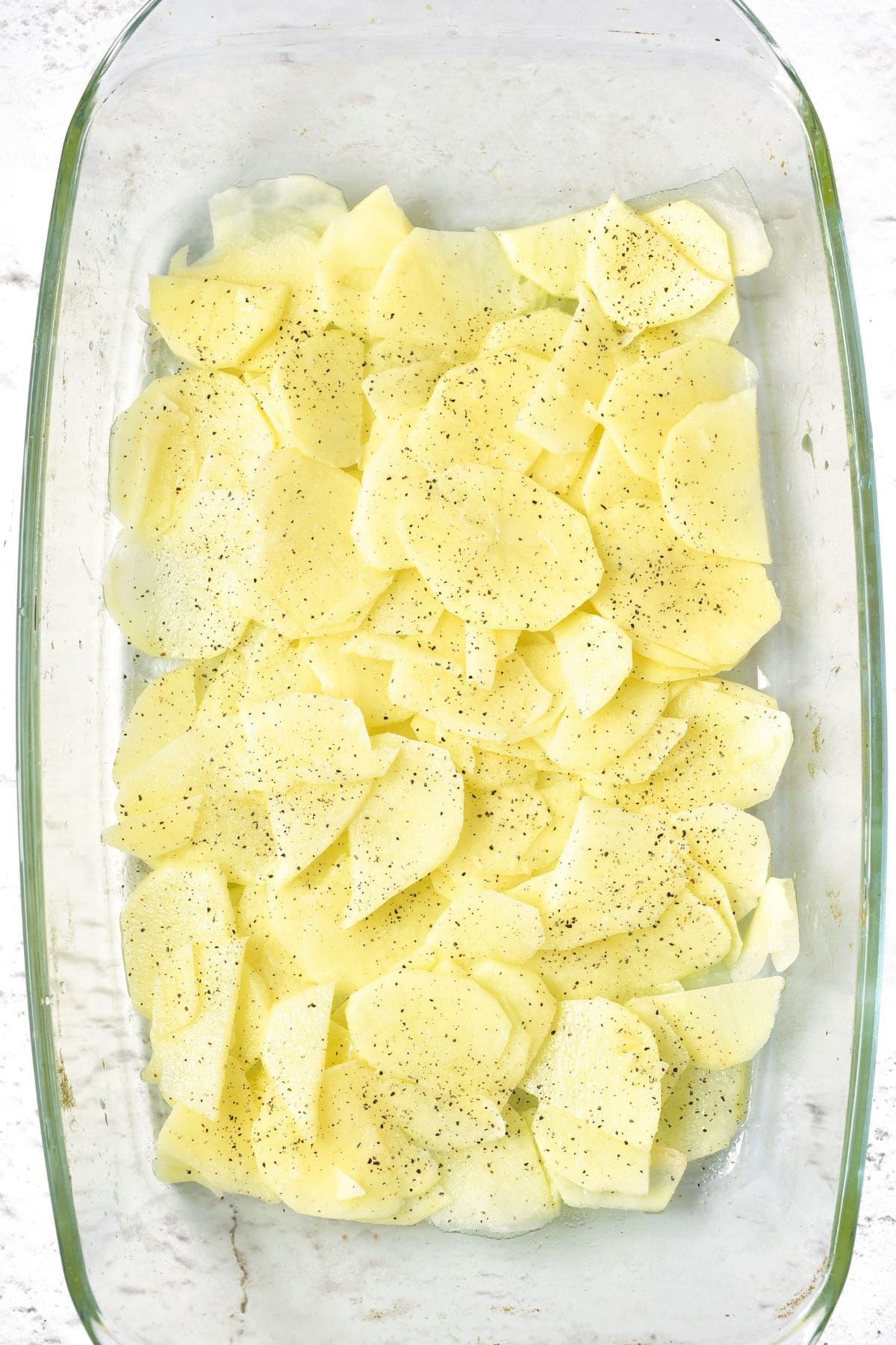 Sliced potatoes sprinkled with pepper in glass casserole dish