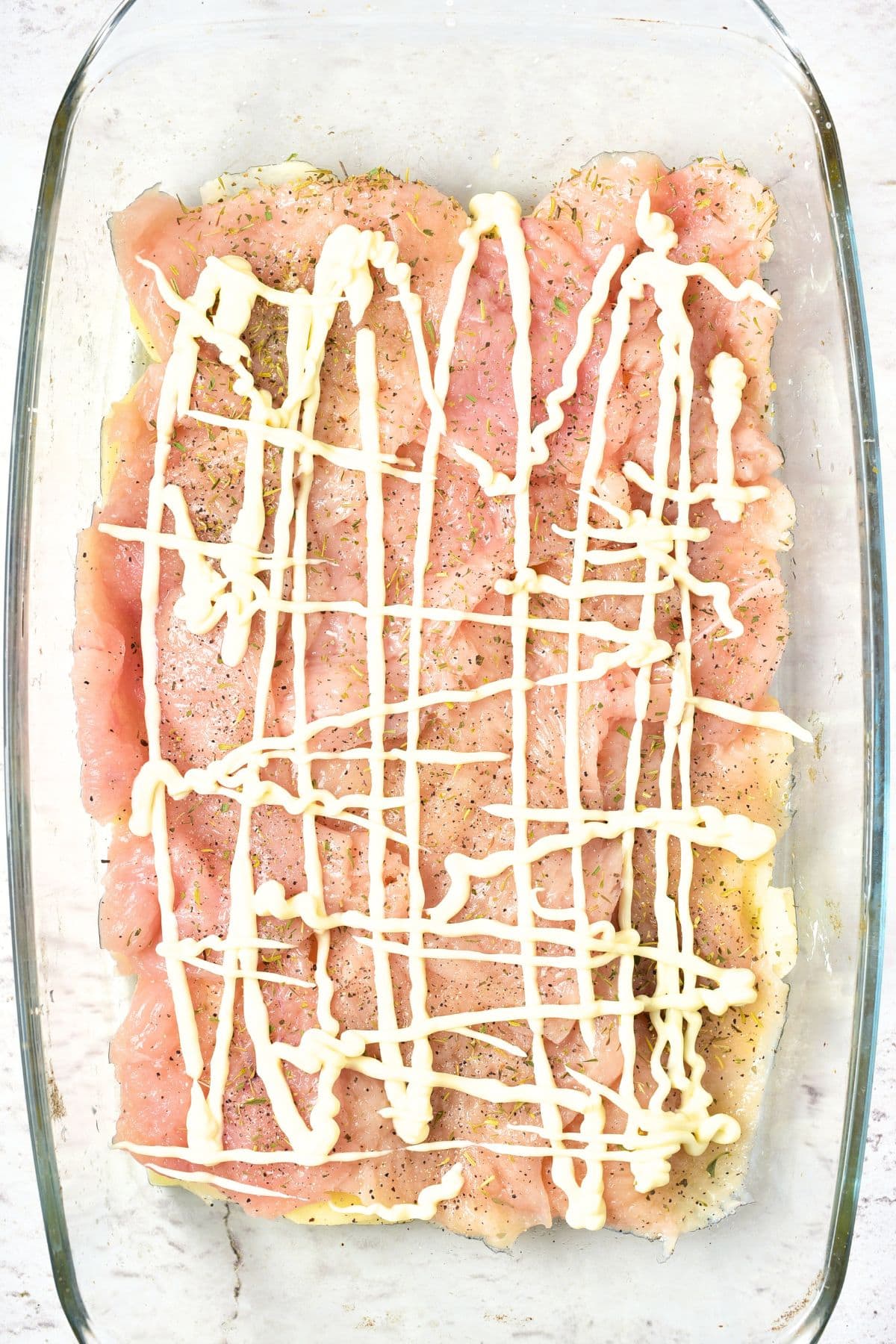 Chicken slices topped with mayonnaise in glass baking dish
