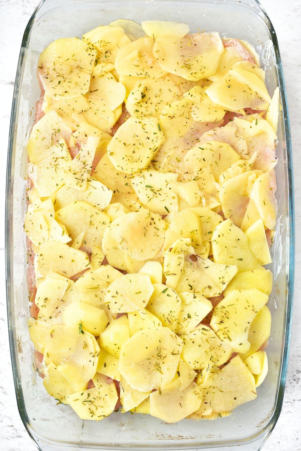 Layers of chicken and potato slices in glass casserole dish