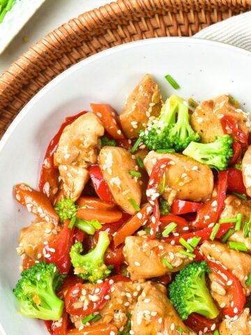 Top down view of a bowl of chicken stir fry on wicker tray