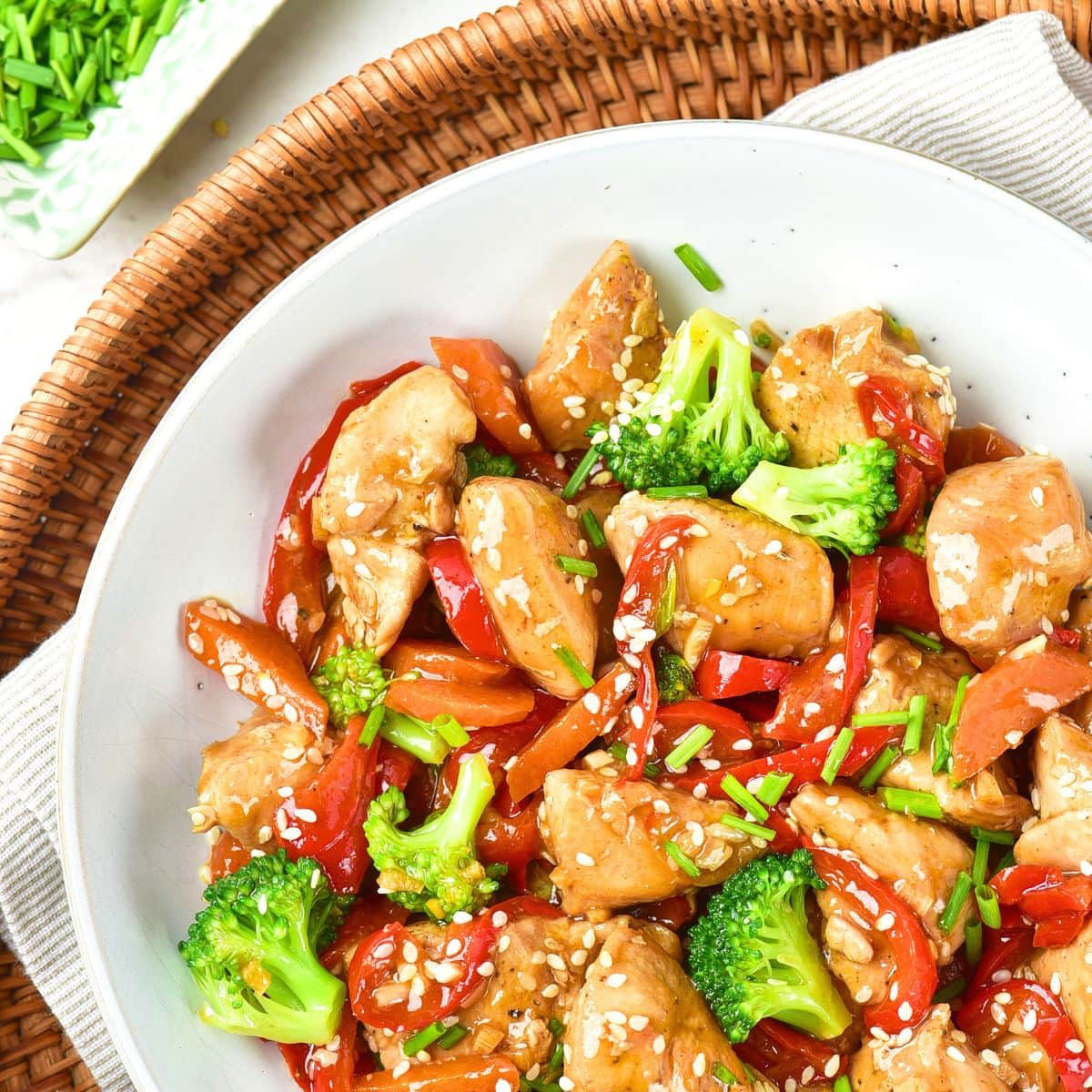 Top down view of a bowl of chicken stir fry on wicker tray