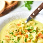 A spoon in bowl of tortellini chicken soup