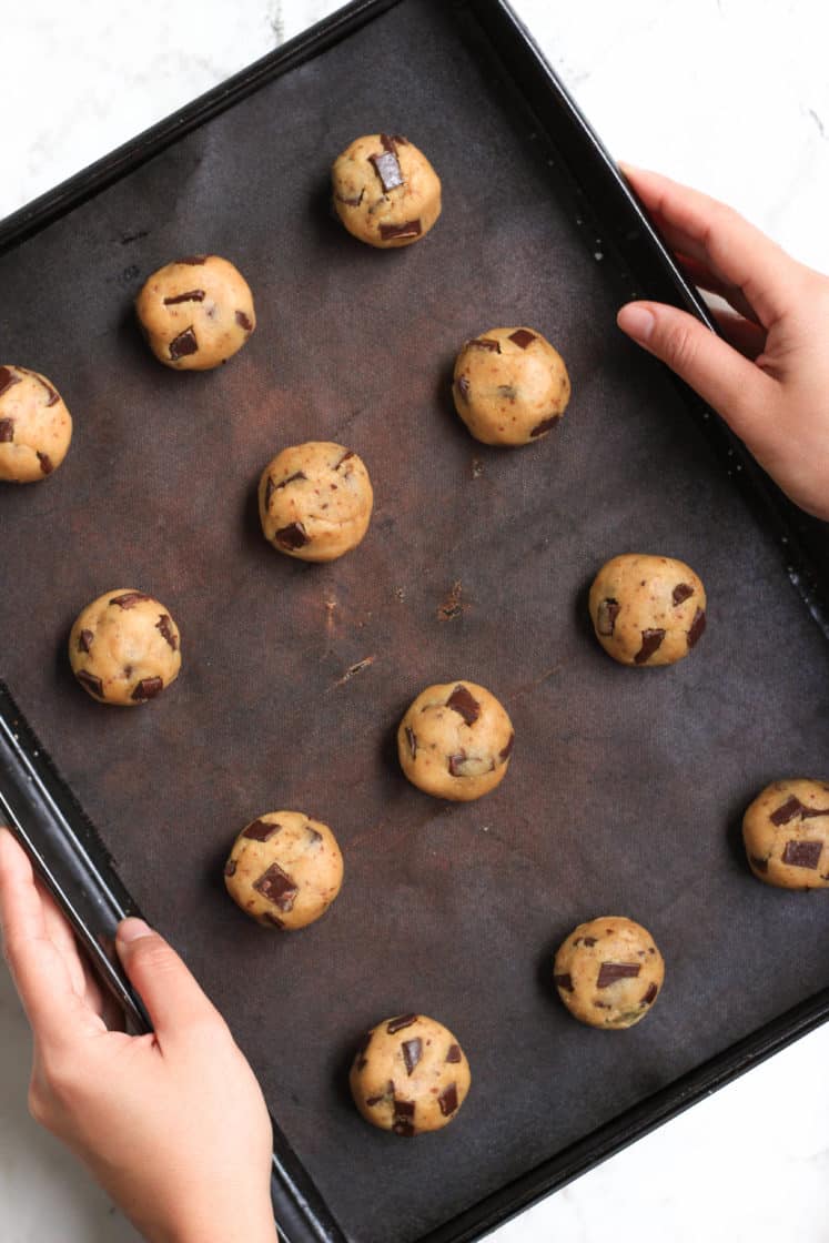 Holding a baking sheet with cookie dough balls on a silpat.