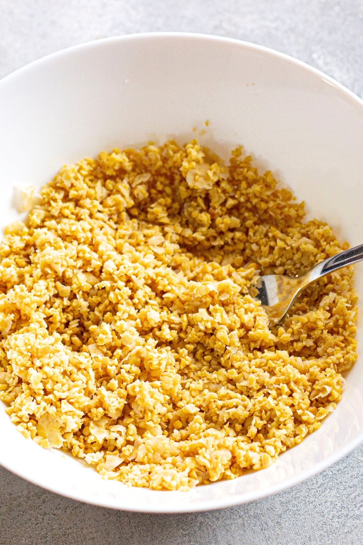 Using a fork to mash chickpeas in white bowl.