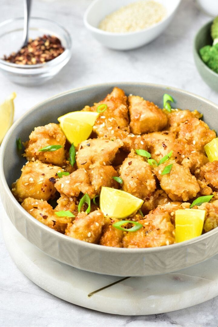 A bowl of lemon chicken with lemon wedges