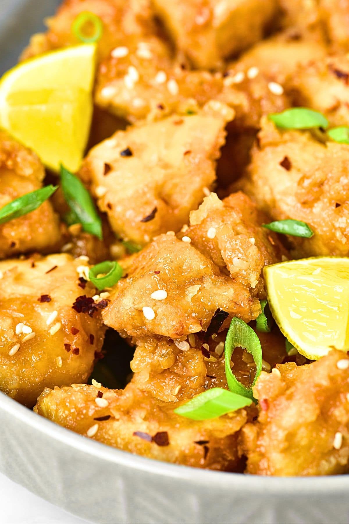 A bowl of gluten-free lemon chicken sprinkled with green onions and sesame seeds.