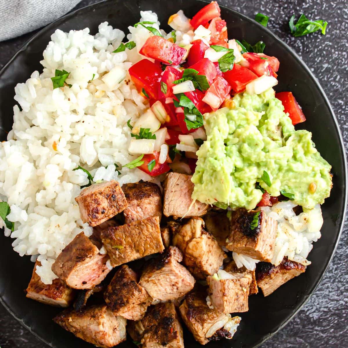Top down view of a bowl with steak bites, guacamole, rice and salsa