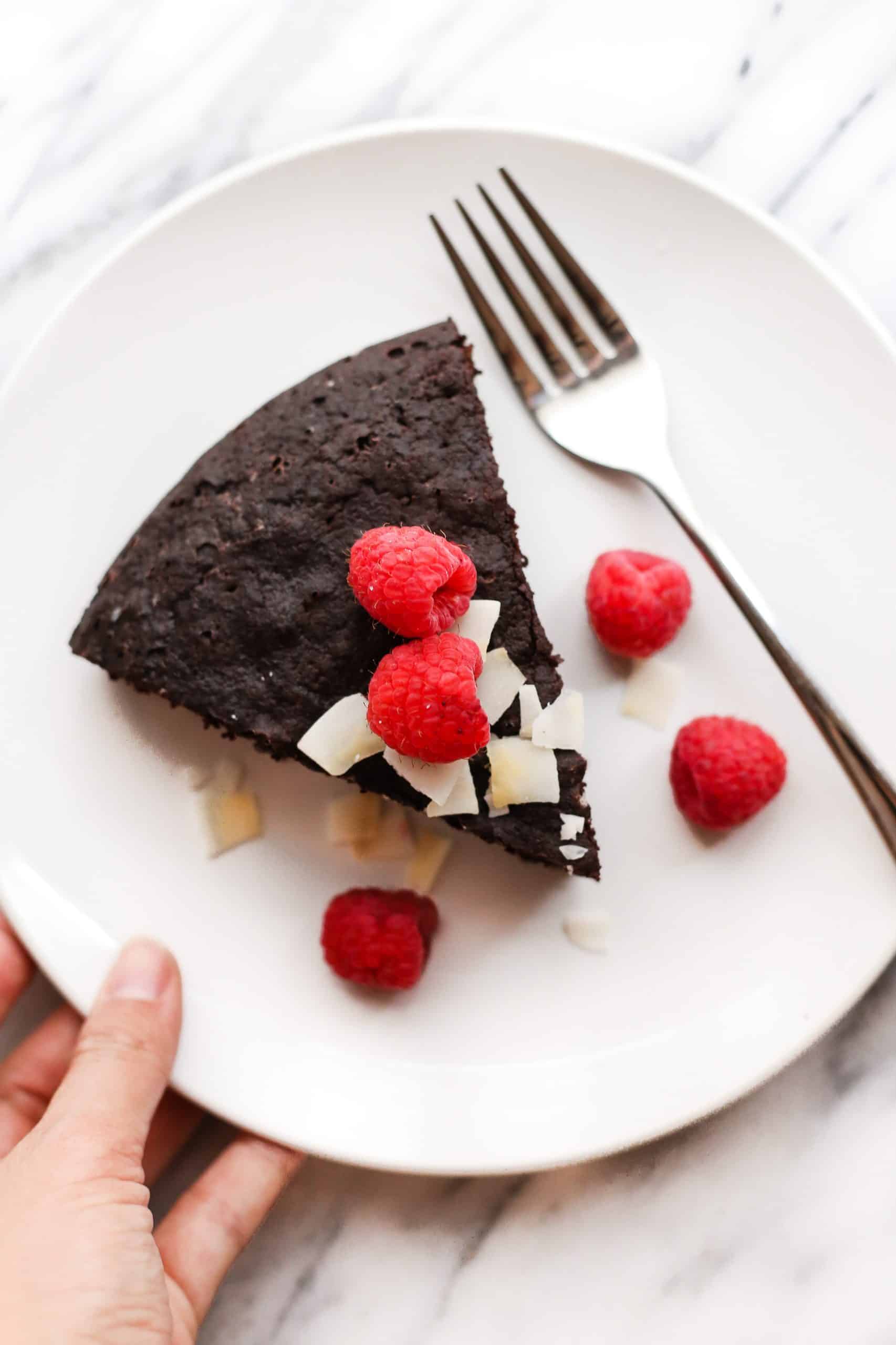Hand holding a plate with a slice of gluten-free chocolate cake.