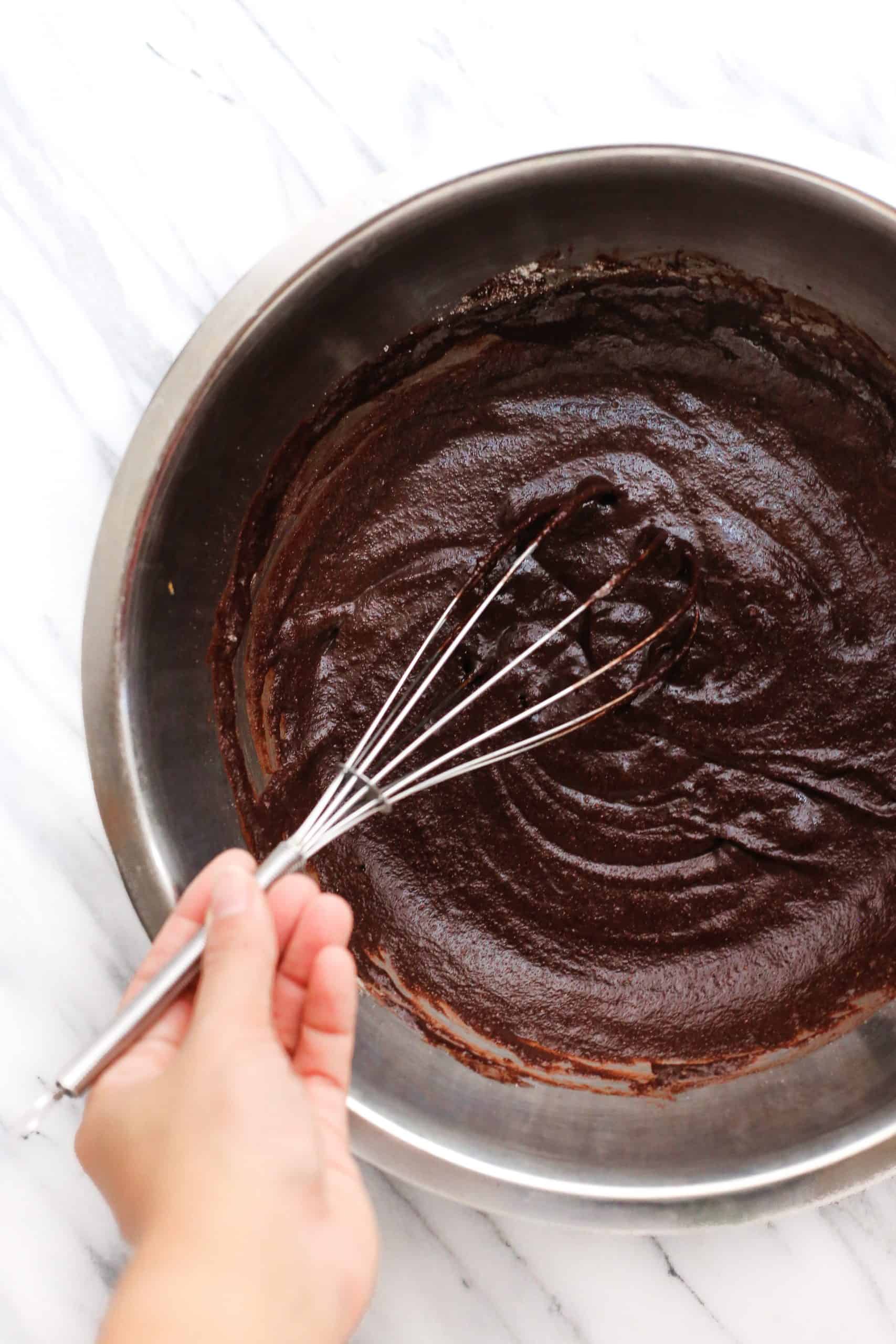 Whisking the flourless chocolate cake batter in a large metal bowl.