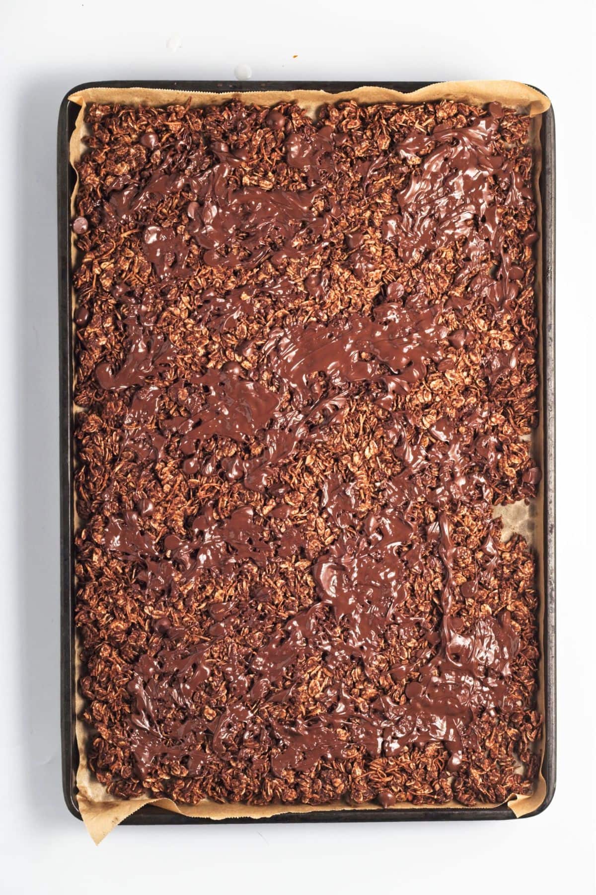 Spreading melted chocolate over granola mixture.