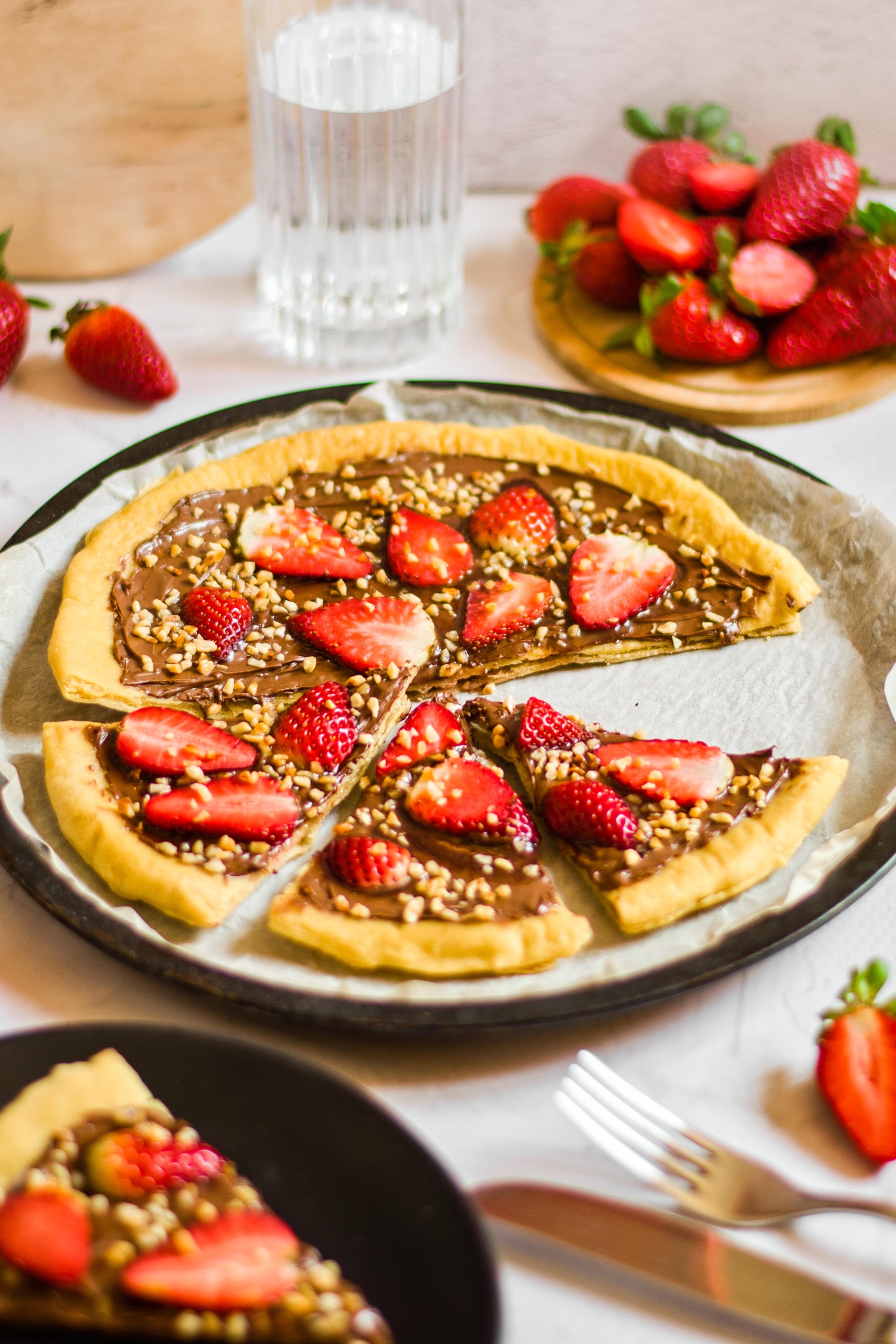 Sliced gluten-free dessert pizza topped with strawberries and hazelnuts. 