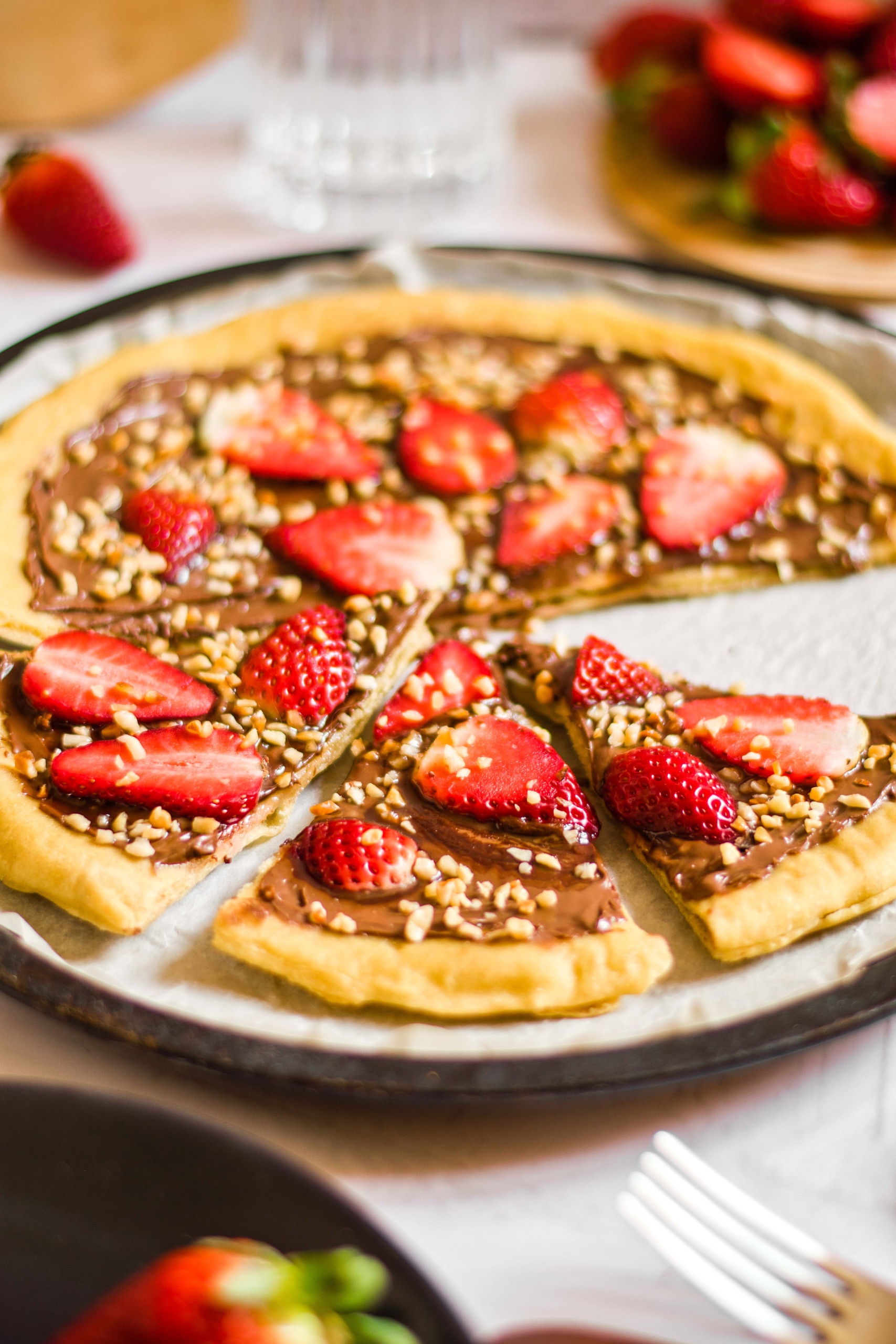 Sliced chocolate dessert pizza topped with strawberries and chopped hazelnuts.