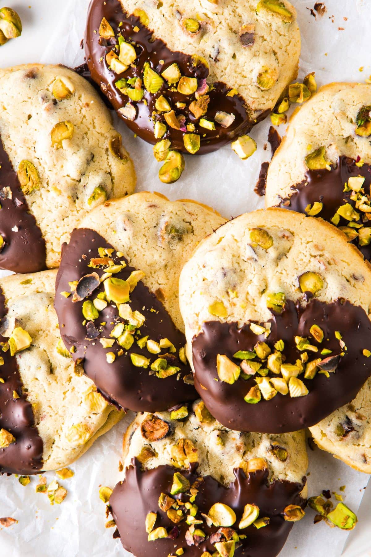 Top down view of chocolate-dipped pistachio cookies on parchment paper.