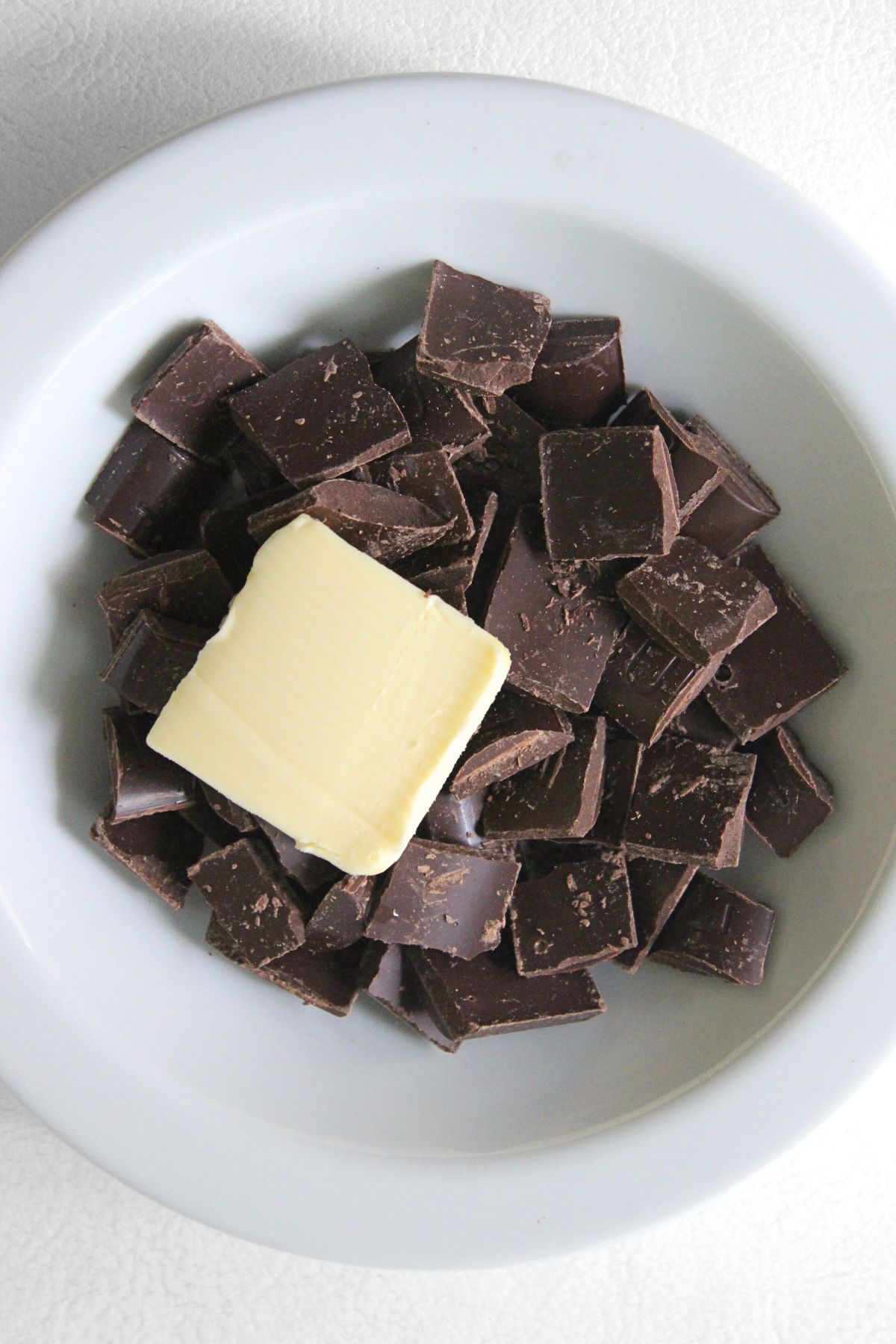 A square of butter on top of chocolate pieces in bowl.