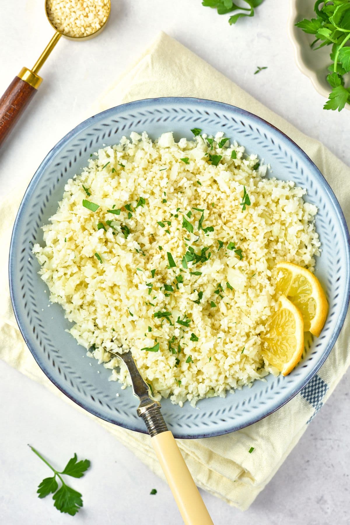 Top down view of a bowl of cilantro cauliflower rice with lemon wedges.