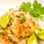A plate of rice and cilantro lime chicken with lime wedges and fresh cilantro