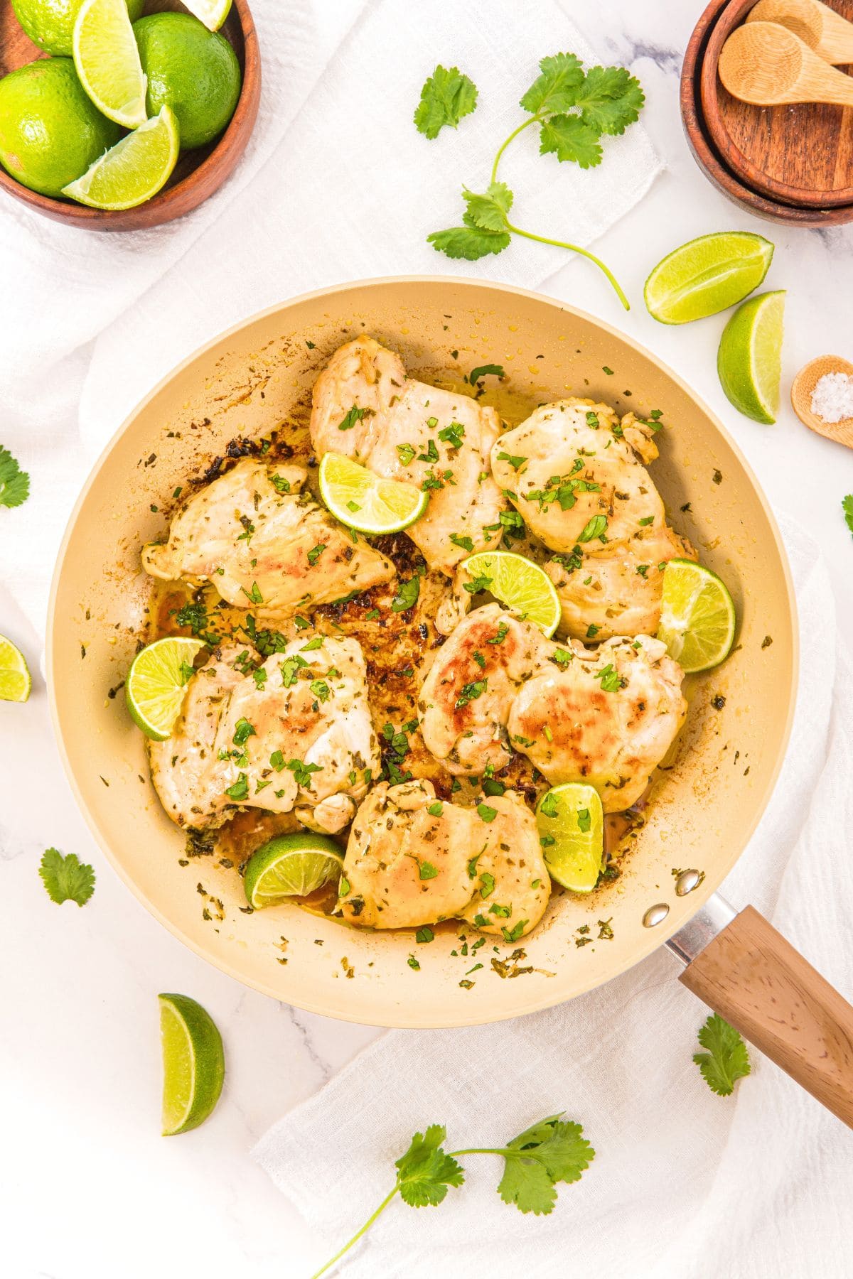 Top down view of a skillet with cilantro lime chicken thighs topped with fresh parsley and lime wedges