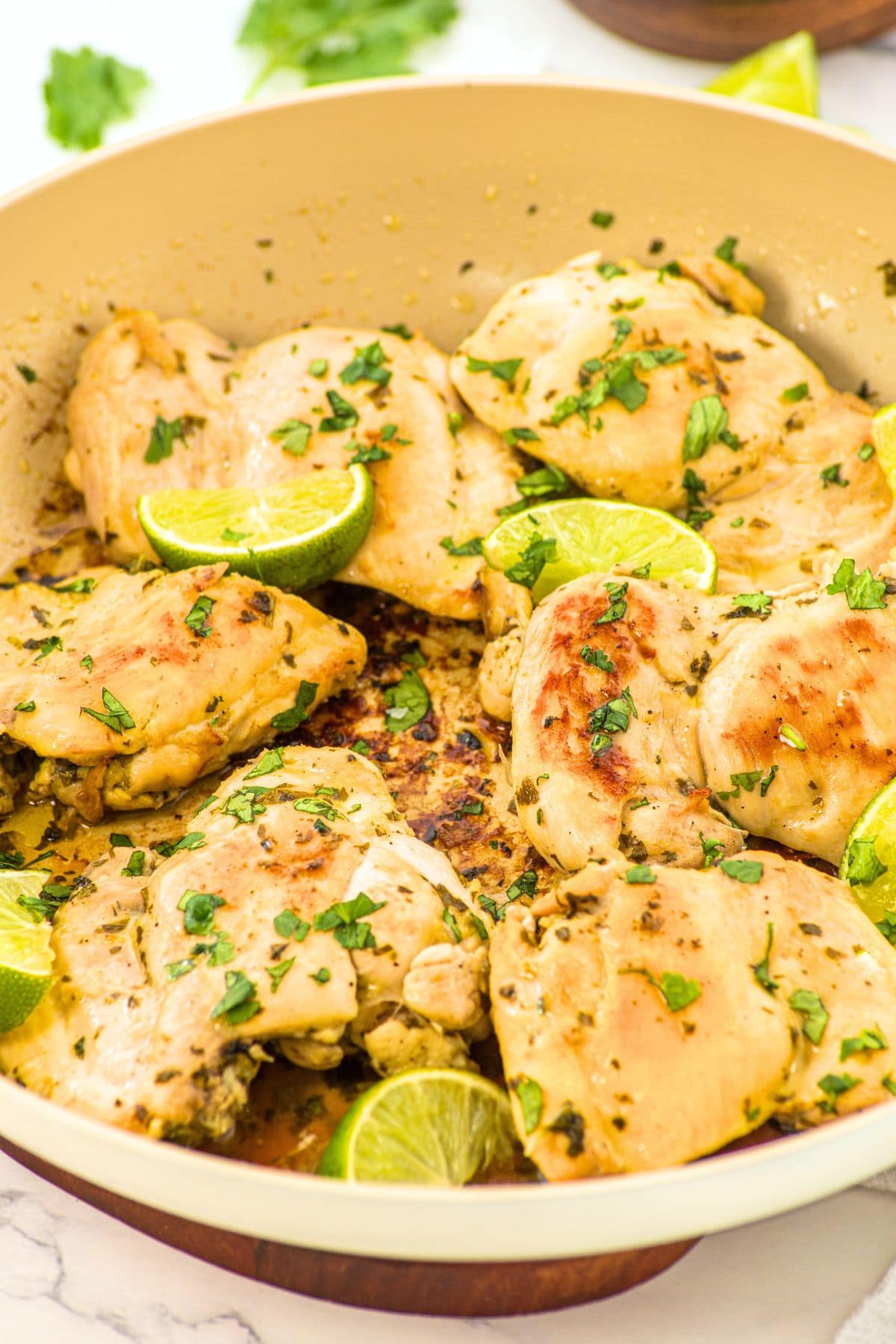 A skillet full of easy cilantro lime chicken topped with lime wedges and chopped cilantro.
