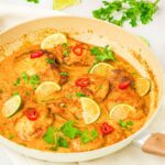 A skillet with coconut lime chicken ganished with fresh cilantro and lime wedges