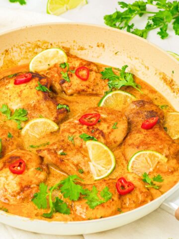 A skillet with coconut lime chicken ganished with fresh cilantro and lime wedges