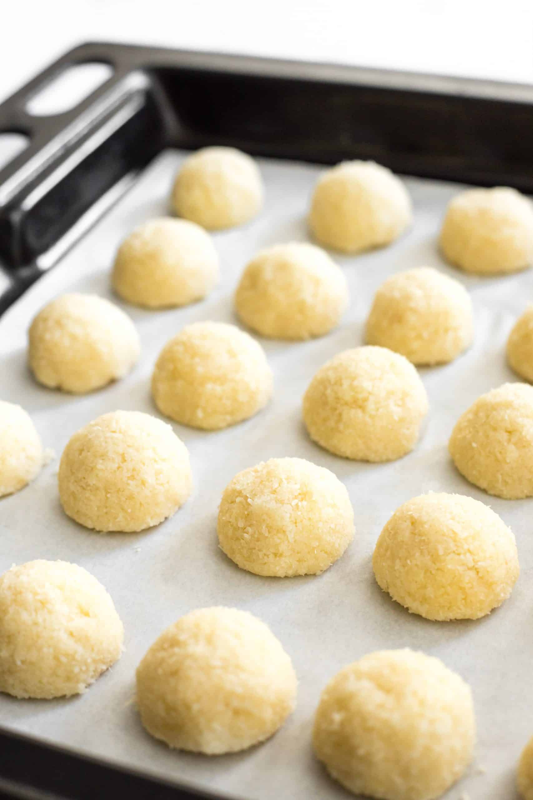 Rows of dome-shaped cookie dough balls on parchment-lined baking sheet.