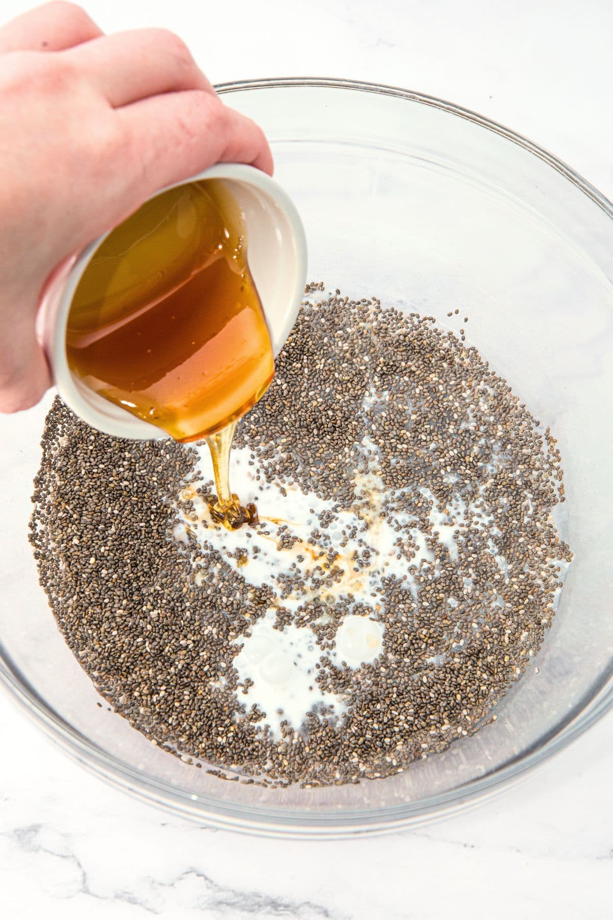 Pouring maple syrup into a bowl of chia seeds and coconut milk.