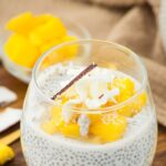 A glass of coconut and chia seed pudding on wooden board
