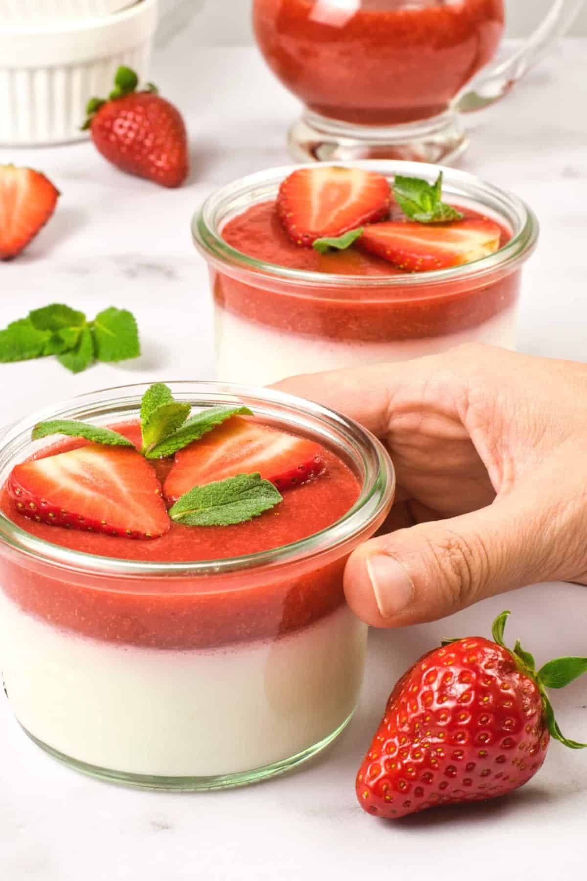 Holding a jar with coconut panna cotta topped with strawberry sauce.