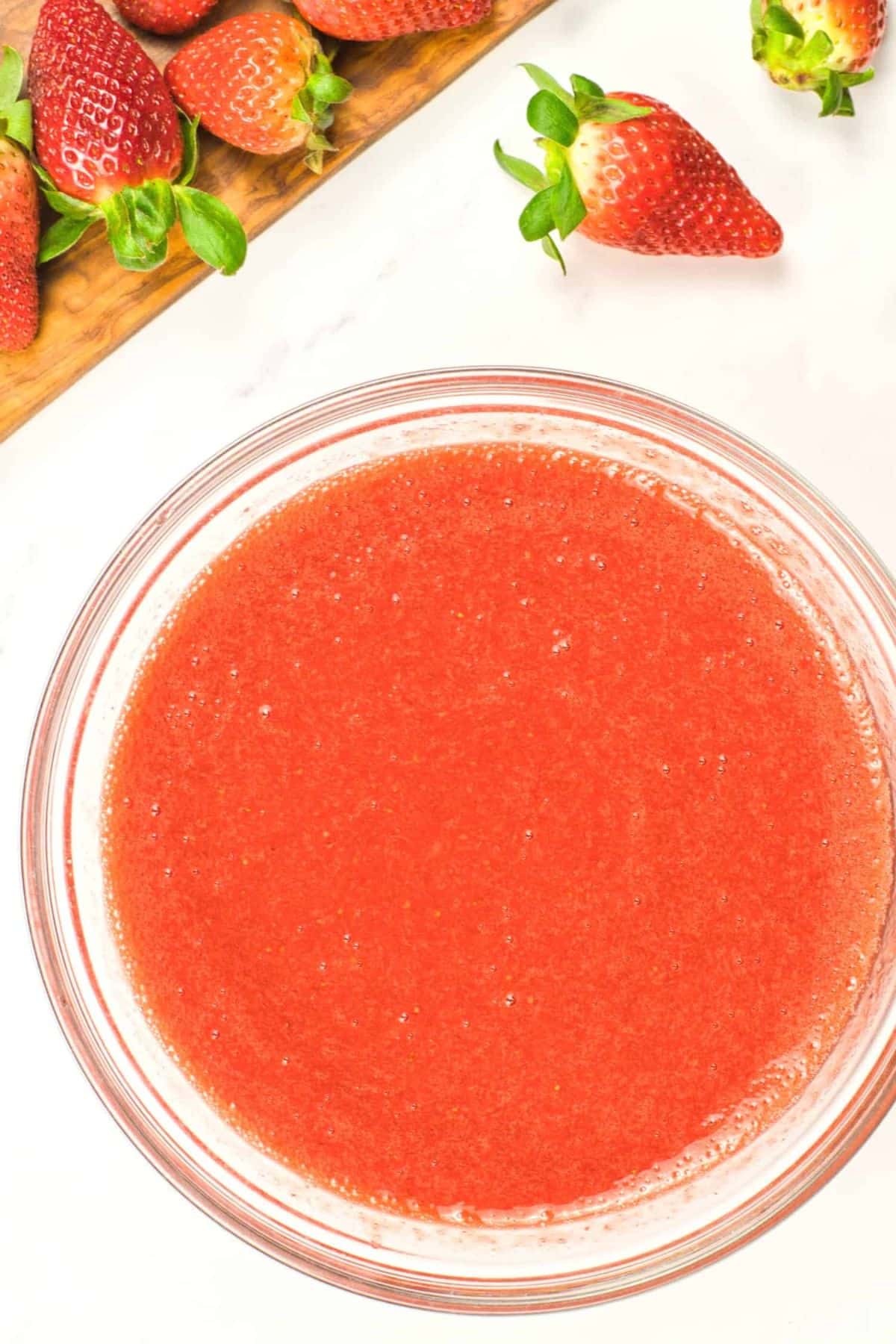 A bowl of strawberry sauce surrounded by fresh strawberries.