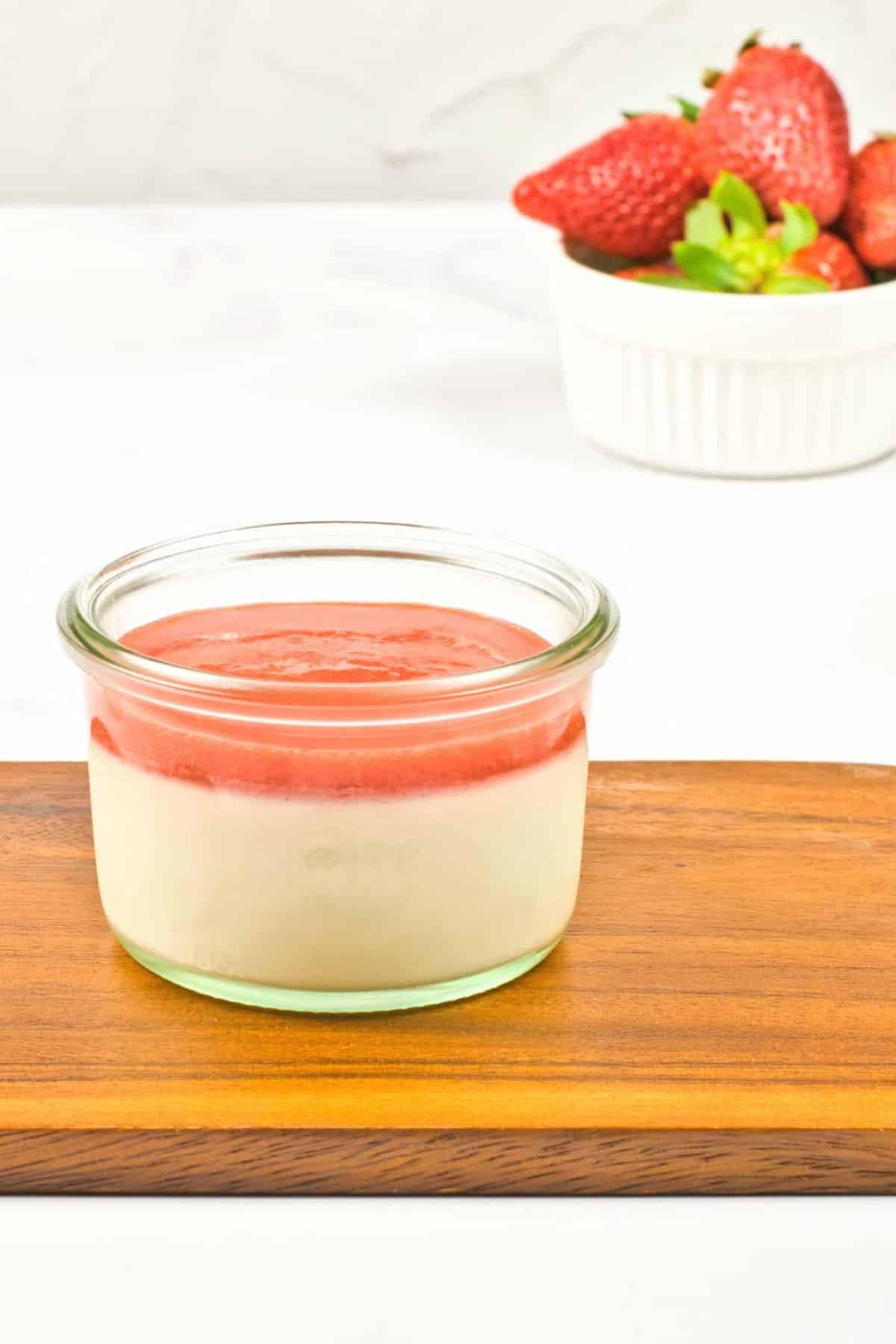 A jar of strawberry panna cotta on wooden board.