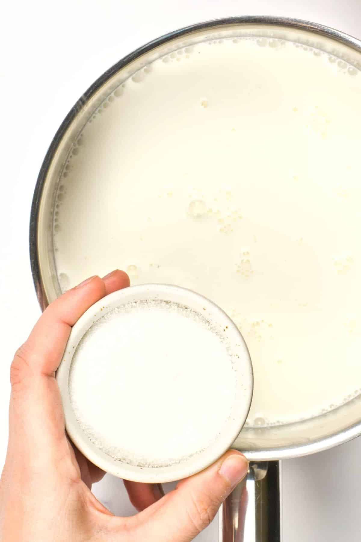 Pouring sugar into a saucepan of coconut milk.