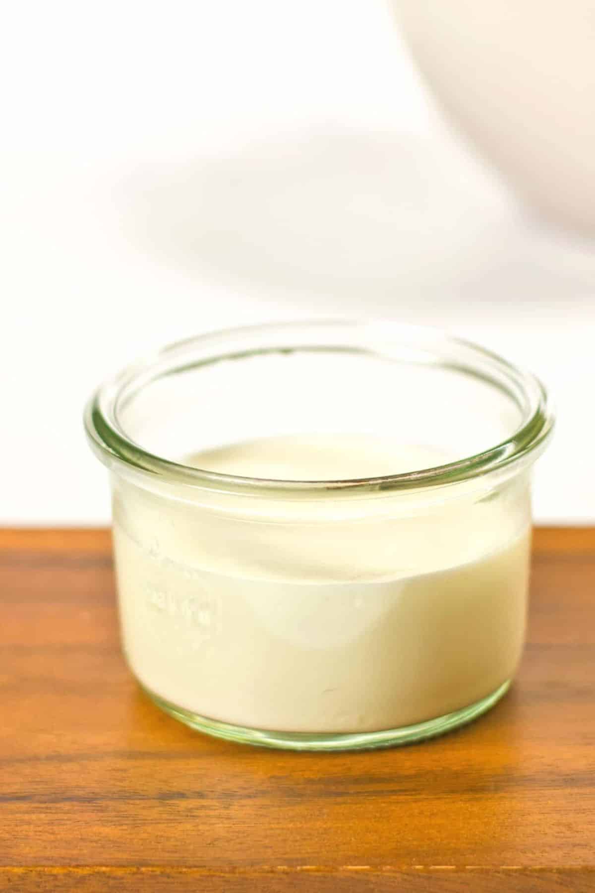 A glass jar of dairy-free panna cotta on wooden board.