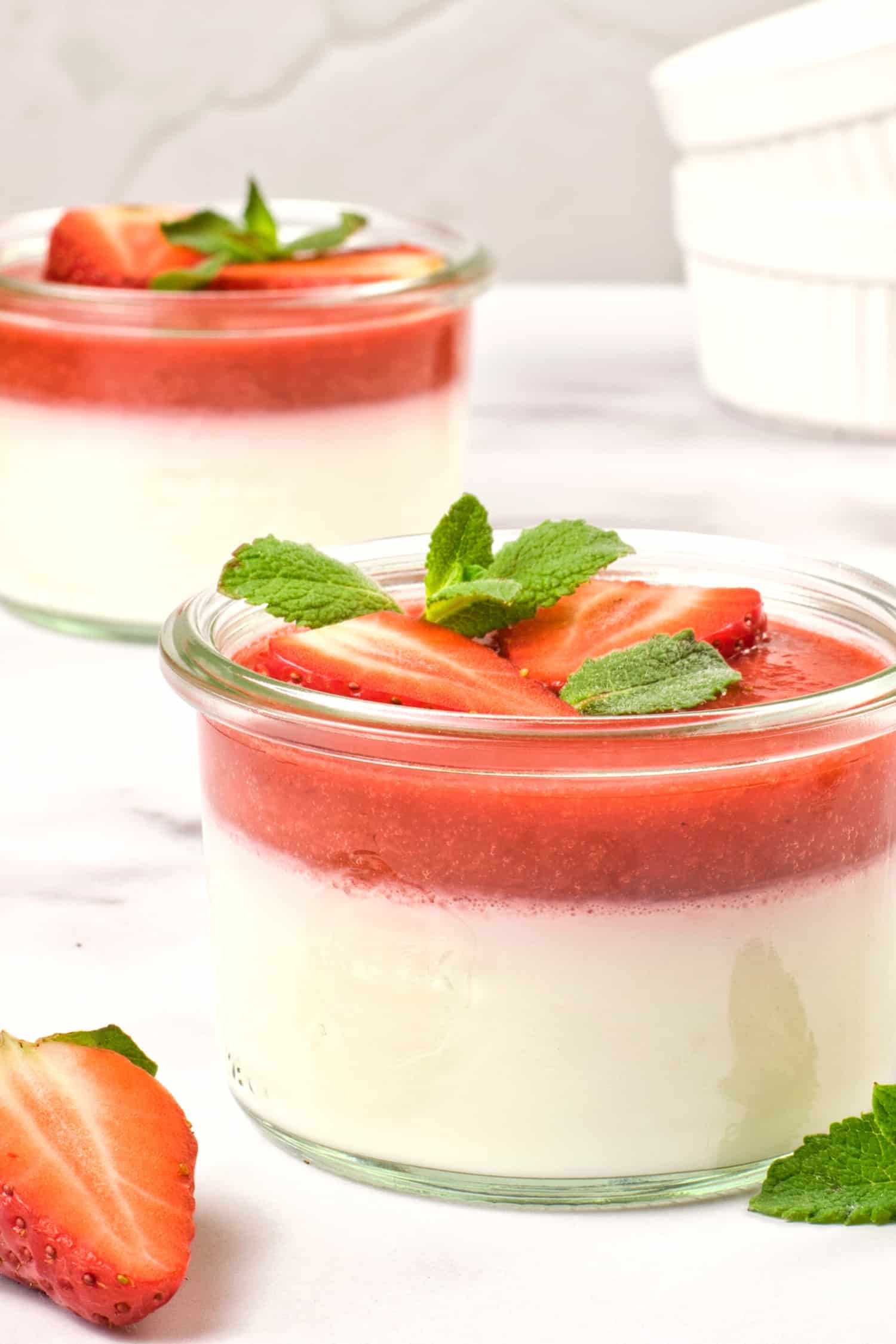 Up close shot of a glass bowl with panna cotta and strawberry sauce.