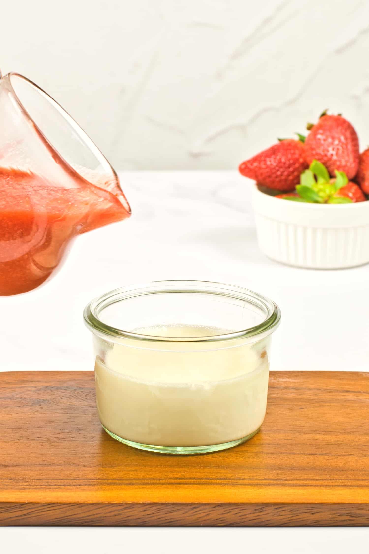 Pouring strawberry sauce over a glass with panna cotta.