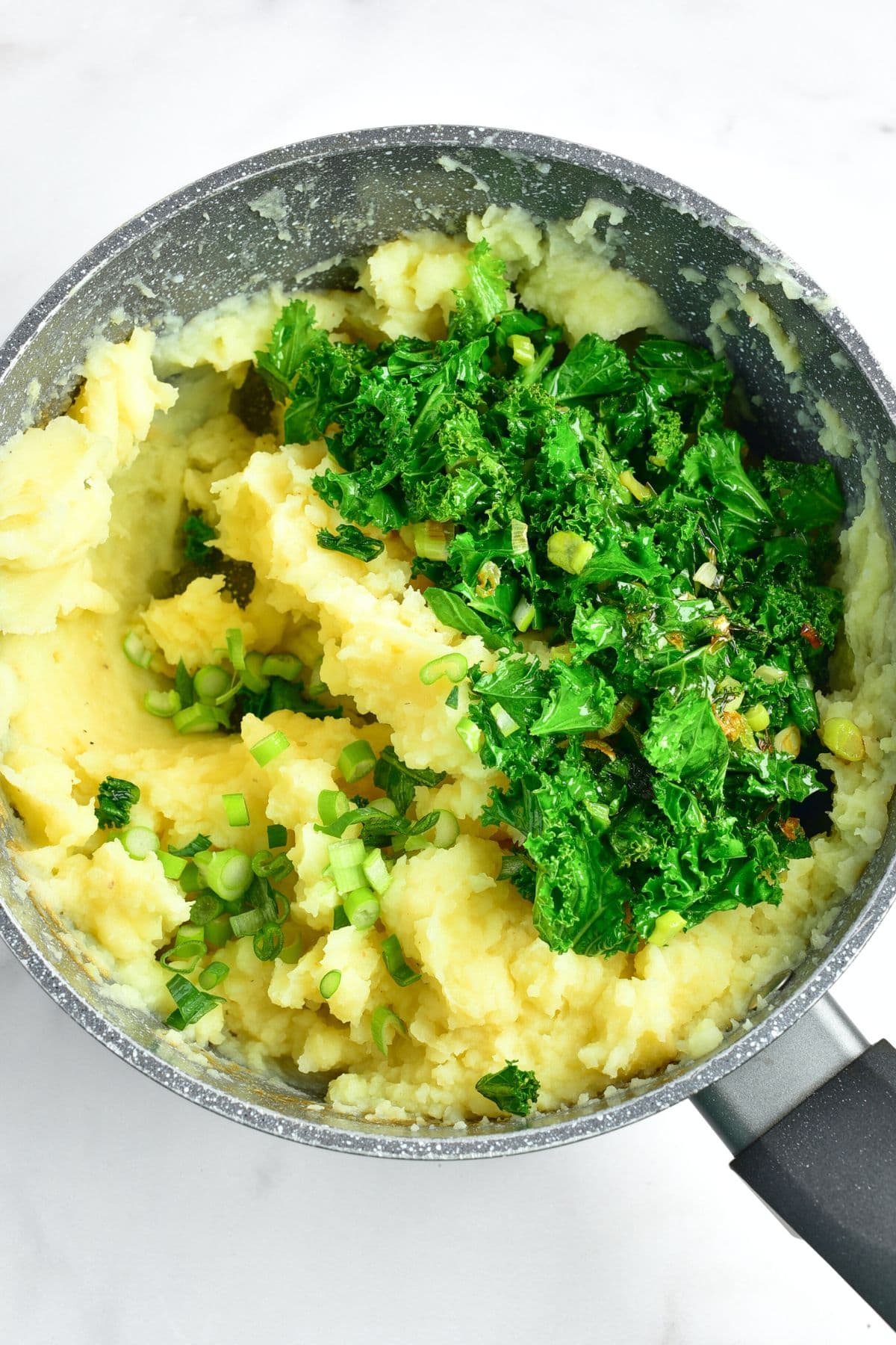 Sautéed kale on top of a pot of mashed potatoes