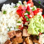 A bowl of chipotle steak bites, rice, guacamole and salsa