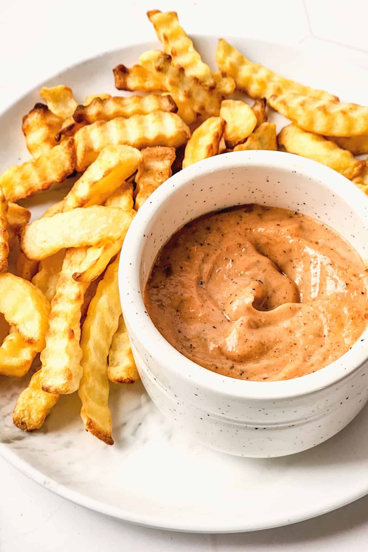 A small bowl of dipping sauce and fries on a white plate.