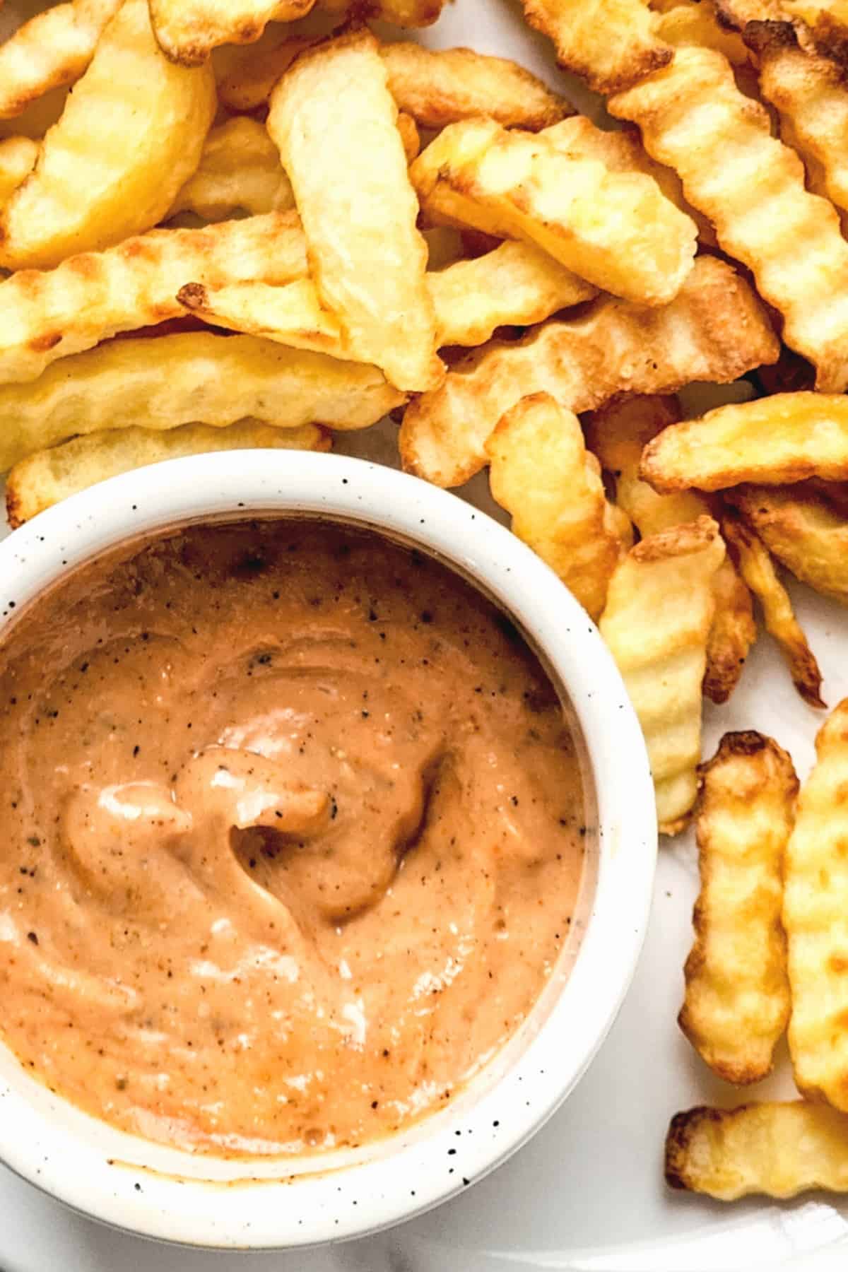 Top down view of a bowl of copycat Raising Cane's sauce surrounded by fries.