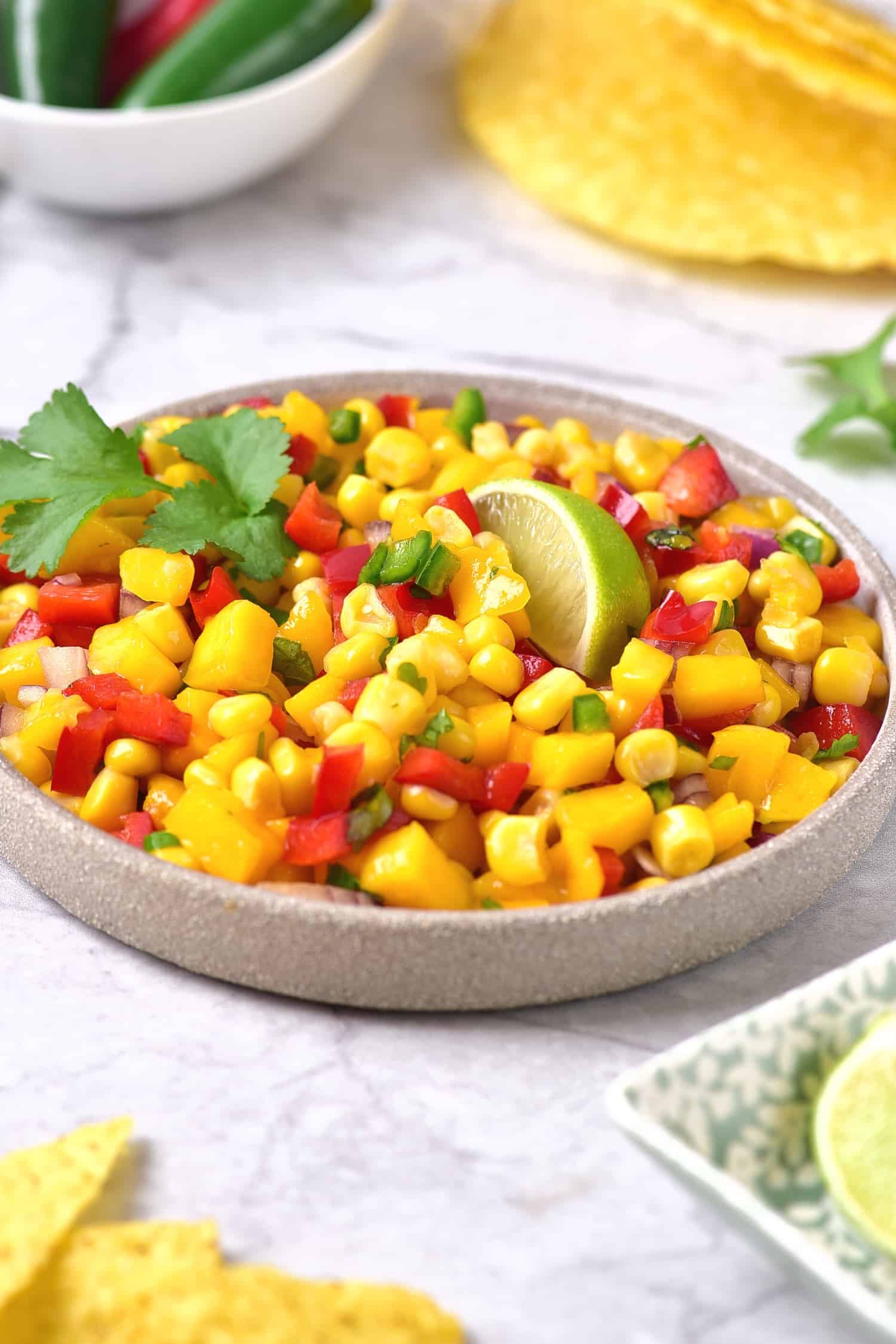 A wedge of lime and freshly cilantro on top of a bowl of mango corn salsa.