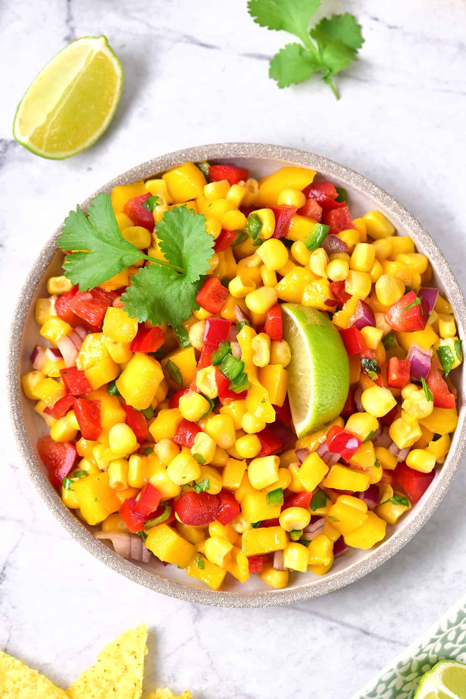 A top down view of a bowl of mango corn salsa on marble board.