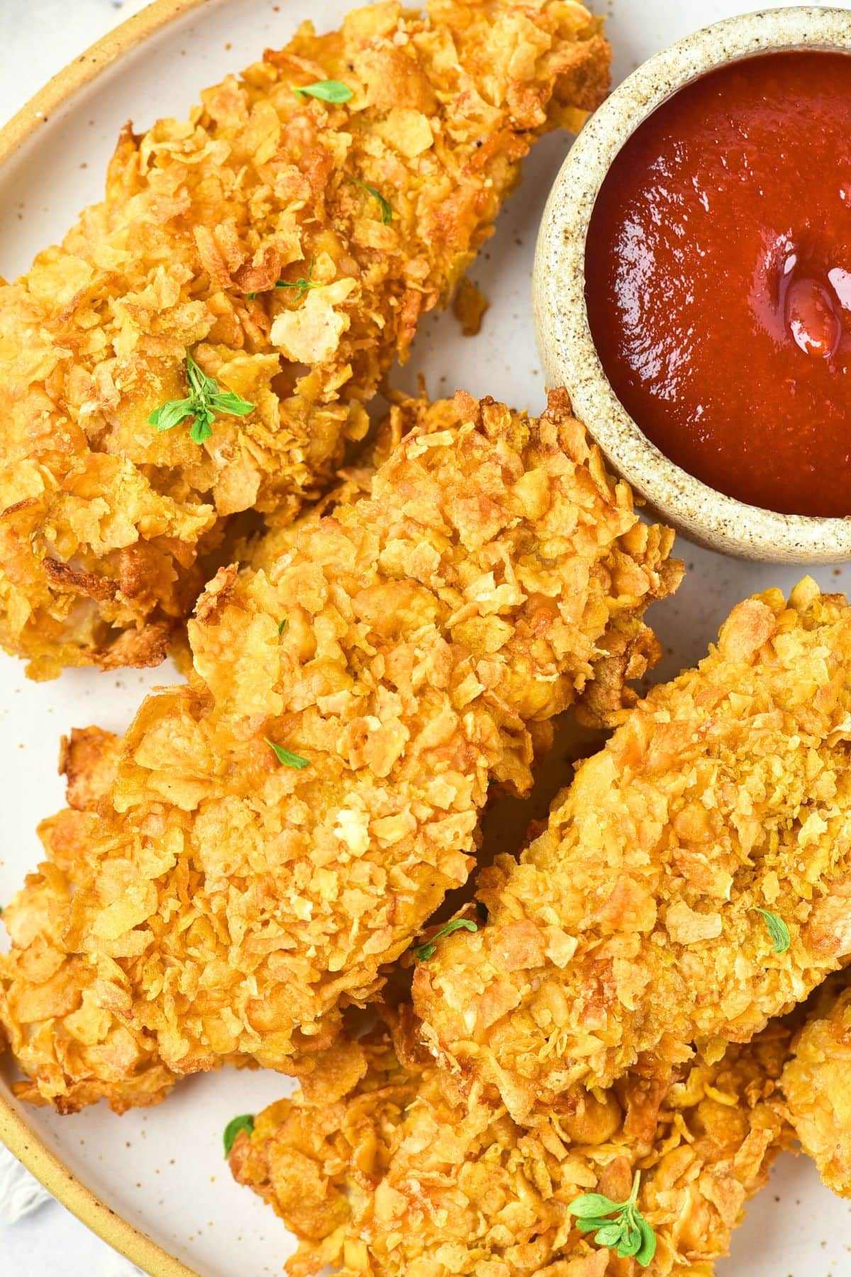 Top down view of baked cornflake chicken strips and ketchup
